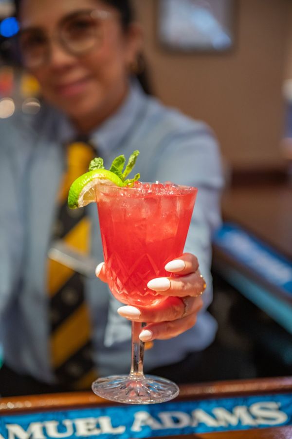 A bartender serving a red cocktail to the camera