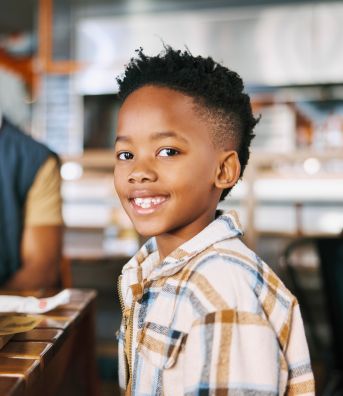 A kid sitting at a table with his family with a burger in front of him